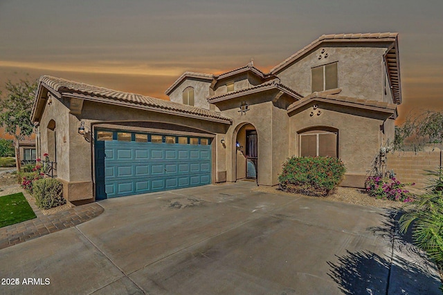 mediterranean / spanish-style home with a garage, driveway, a tiled roof, and stucco siding