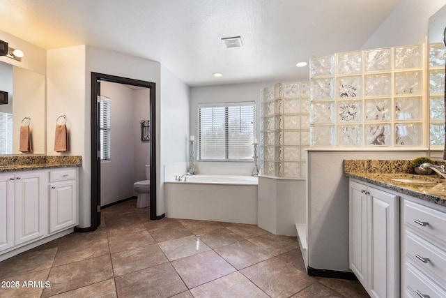 full bathroom with toilet, two vanities, visible vents, a sink, and a bath