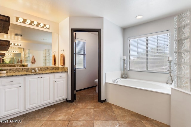 full bathroom featuring a healthy amount of sunlight, a garden tub, toilet, and vanity