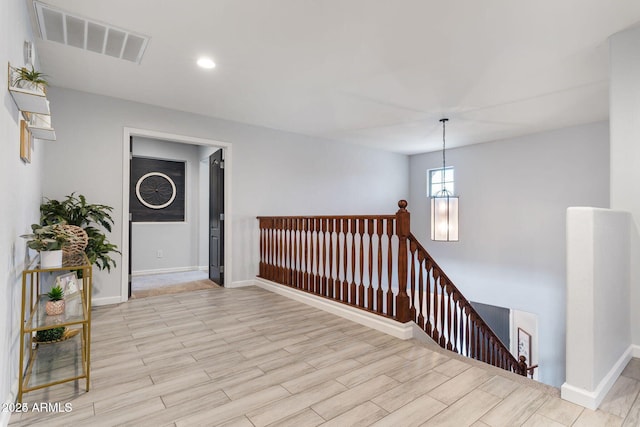 hallway with baseboards, visible vents, an upstairs landing, light wood-type flooring, and recessed lighting