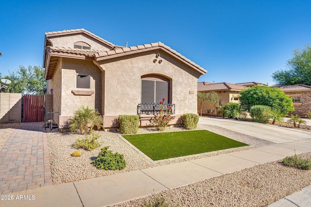 mediterranean / spanish-style home with a gate, fence, a tiled roof, and stucco siding