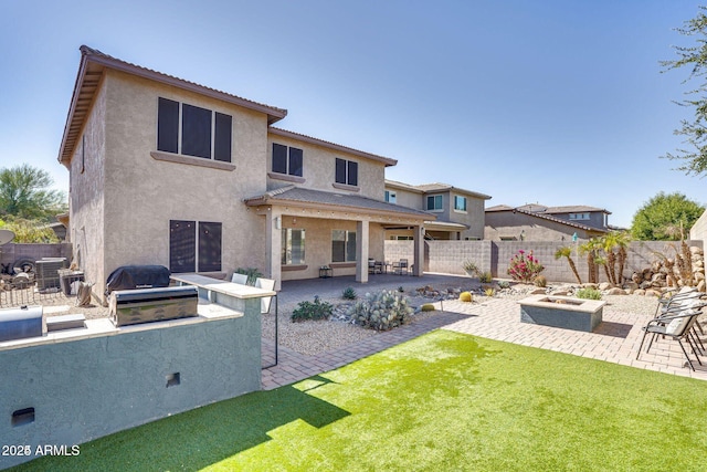 back of house featuring an outdoor fire pit, a fenced backyard, a patio, and an outdoor kitchen