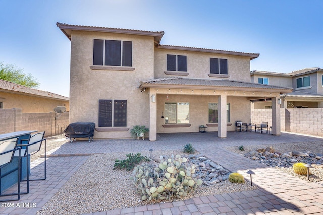 rear view of house with a patio, fence, and stucco siding