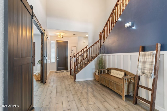 entryway with a wainscoted wall, stairway, a towering ceiling, a barn door, and light wood-type flooring