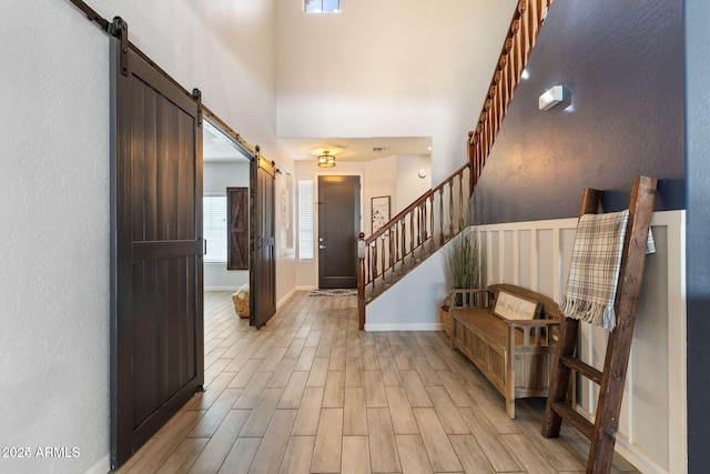 foyer with light wood finished floors, a barn door, baseboards, a towering ceiling, and stairs