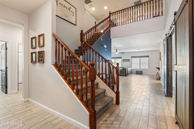 stairs featuring wood finish floors, a high ceiling, a barn door, a ceiling fan, and baseboards