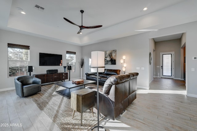 living room featuring a raised ceiling, ceiling fan, and light hardwood / wood-style floors