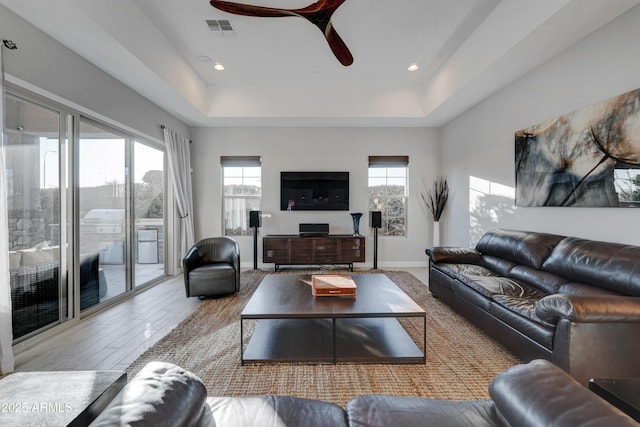 living room featuring a raised ceiling, ceiling fan, and light hardwood / wood-style flooring