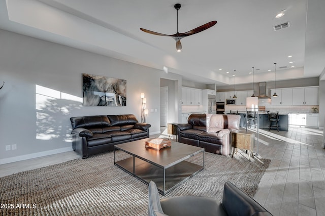 living room with light hardwood / wood-style flooring, a raised ceiling, and ceiling fan