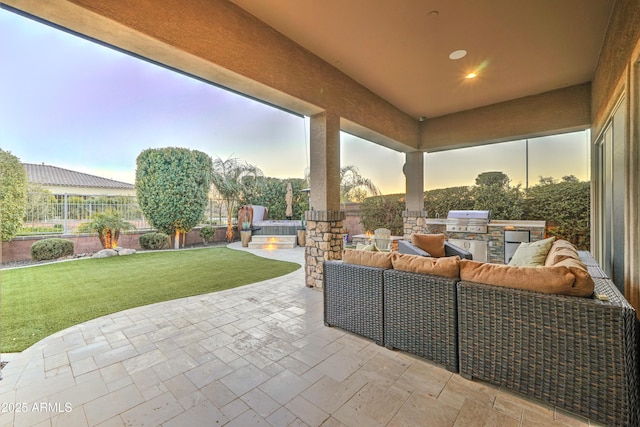 patio terrace at dusk with area for grilling, an outdoor living space, a lawn, and an outdoor kitchen