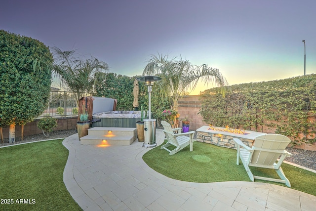 patio terrace at dusk with a hot tub, a fire pit, and a lawn