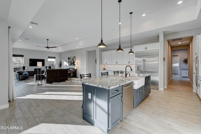 kitchen with white cabinetry, decorative light fixtures, a center island with sink, a tray ceiling, and stainless steel appliances