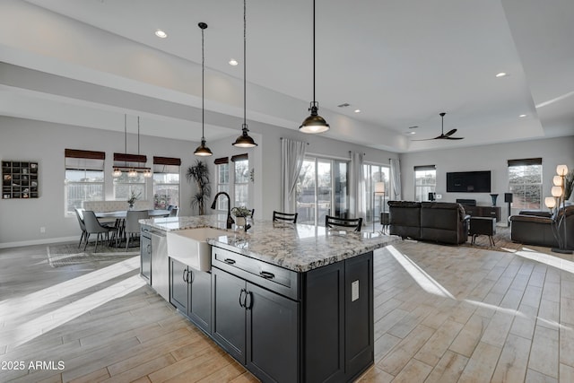 kitchen with pendant lighting, sink, a tray ceiling, light stone countertops, and an island with sink