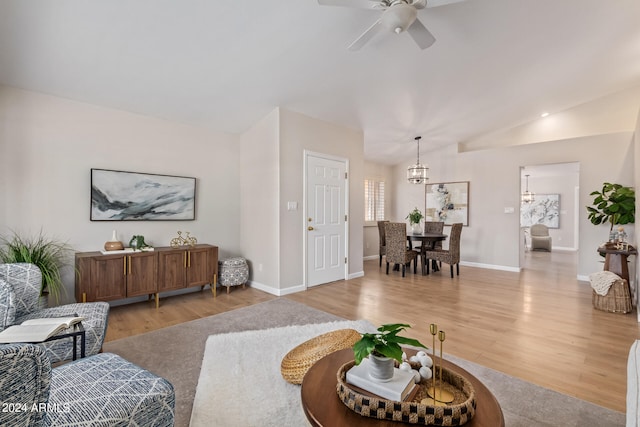 living room featuring light wood-type flooring, ceiling fan with notable chandelier, and vaulted ceiling