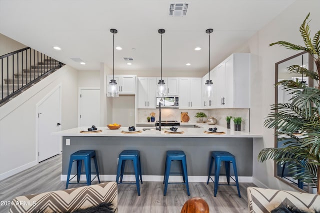 kitchen featuring kitchen peninsula, decorative light fixtures, decorative backsplash, a kitchen bar, and white cabinets