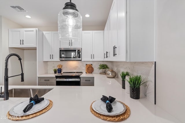 kitchen with sink, white cabinets, backsplash, hanging light fixtures, and appliances with stainless steel finishes