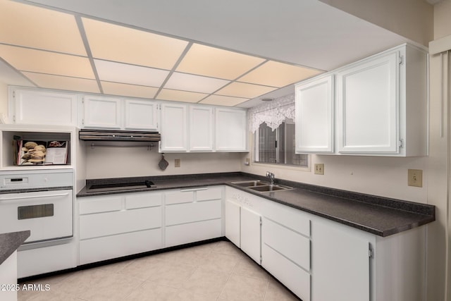 kitchen featuring white oven, dark countertops, white cabinetry, a sink, and stovetop