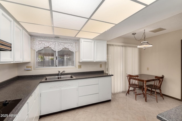 kitchen with black electric stovetop, dark countertops, visible vents, white cabinetry, and a sink