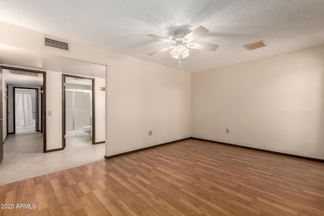 spare room featuring a ceiling fan, visible vents, a textured ceiling, and light wood finished floors