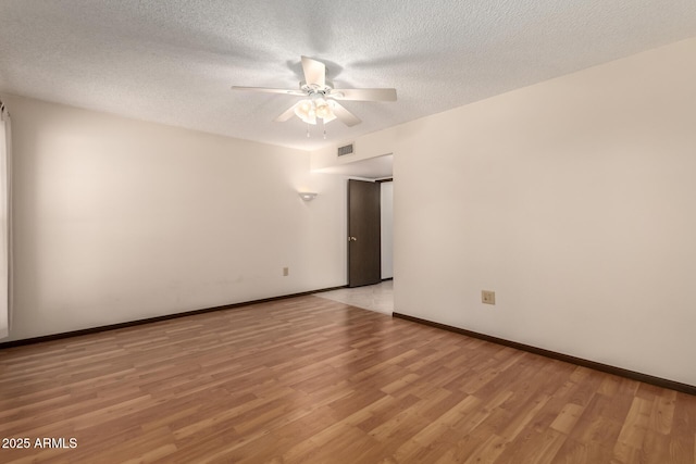 spare room featuring light wood finished floors, baseboards, visible vents, a ceiling fan, and a textured ceiling