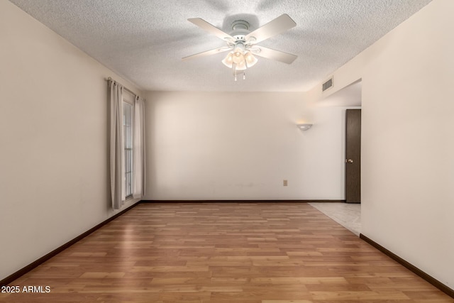 spare room with light wood-type flooring, visible vents, ceiling fan, and baseboards