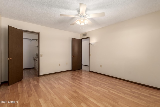 unfurnished bedroom with a textured ceiling, visible vents, baseboards, light wood-type flooring, and a walk in closet