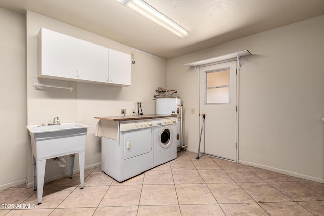 washroom with light tile patterned flooring, baseboards, water heater, cabinet space, and washing machine and clothes dryer