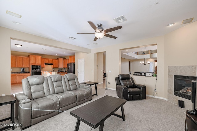 living room with light carpet, ceiling fan with notable chandelier, and a tiled fireplace