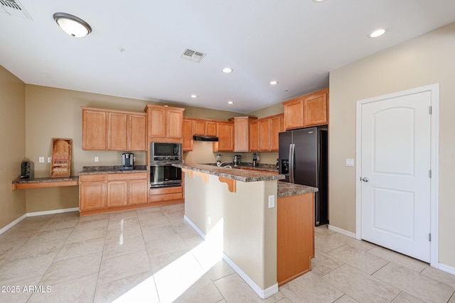 kitchen featuring appliances with stainless steel finishes, light tile patterned floors, dark stone countertops, a kitchen island, and a breakfast bar area