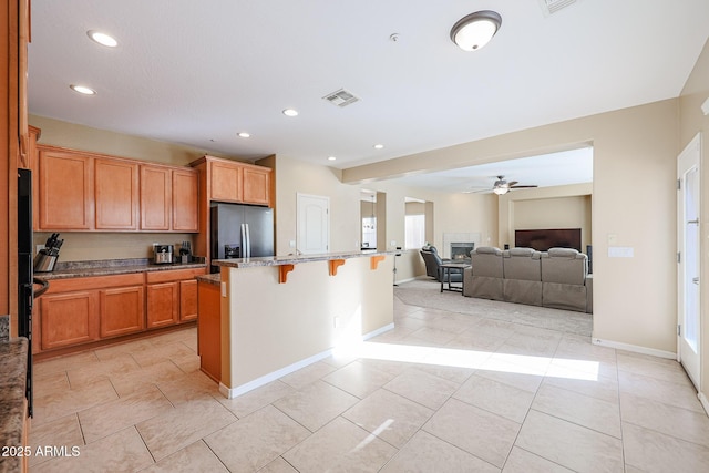 kitchen featuring a kitchen breakfast bar, ceiling fan, stainless steel fridge with ice dispenser, and a kitchen island with sink