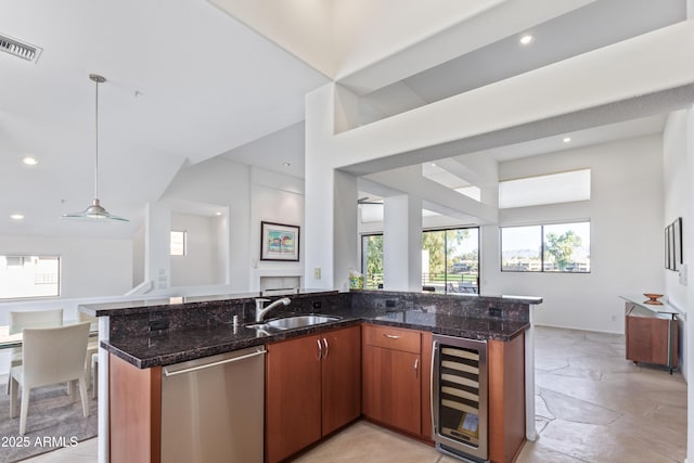 kitchen featuring sink, dishwasher, beverage cooler, dark stone counters, and hanging light fixtures