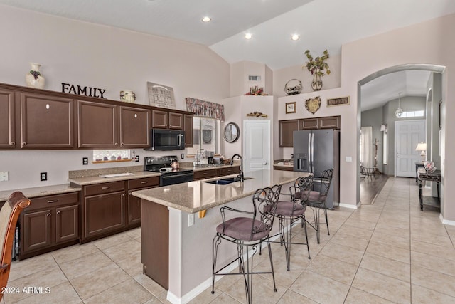 kitchen featuring light stone countertops, a breakfast bar, black appliances, sink, and an island with sink