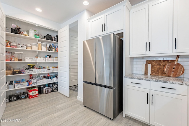 kitchen with tasteful backsplash, light stone countertops, freestanding refrigerator, white cabinets, and open shelves