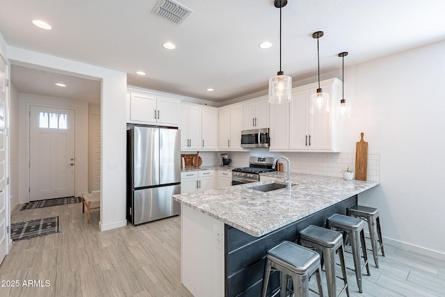 kitchen featuring a sink, white cabinetry, stainless steel appliances, a peninsula, and decorative backsplash