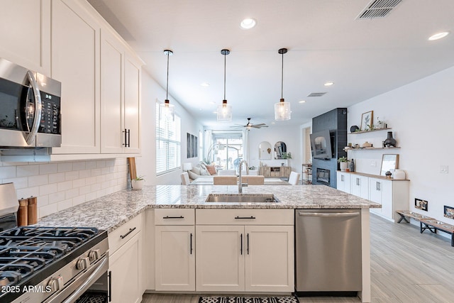 kitchen with visible vents, a peninsula, a sink, appliances with stainless steel finishes, and backsplash