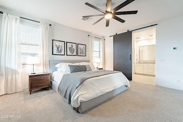 bedroom featuring a ceiling fan, ensuite bath, a barn door, baseboards, and light colored carpet