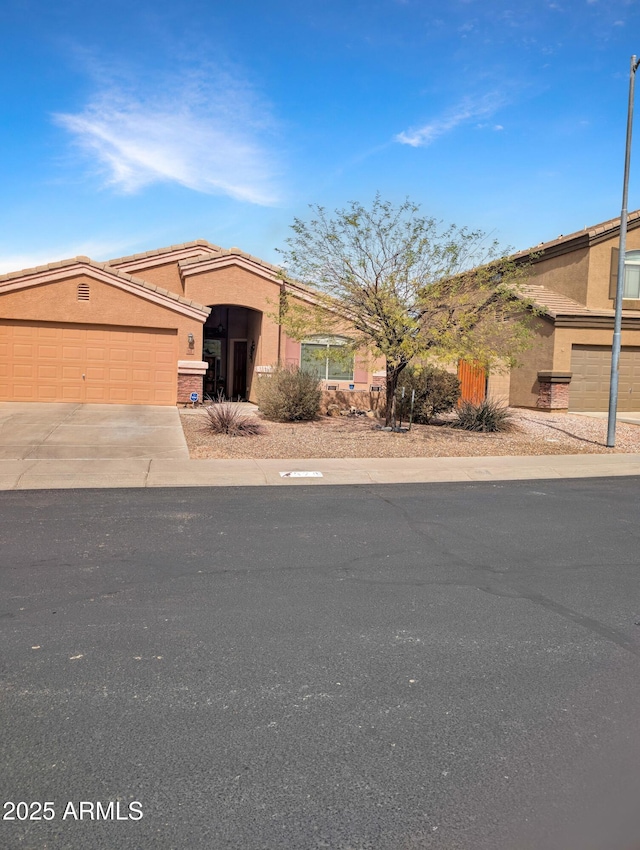 view of front of house with concrete driveway, a tiled roof, an attached garage, and stucco siding