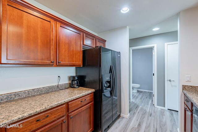 kitchen featuring light wood-type flooring, stone countertops, and black fridge