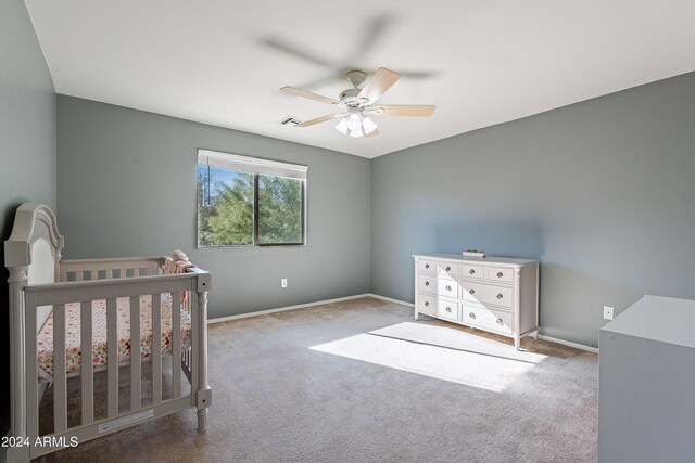 carpeted bedroom with ceiling fan and a nursery area