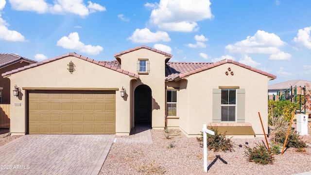 mediterranean / spanish home with a garage, a tiled roof, decorative driveway, and stucco siding