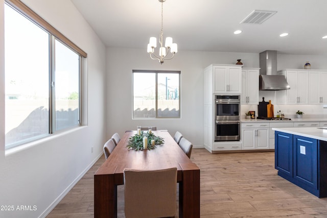 kitchen featuring blue cabinetry, stainless steel appliances, white cabinets, decorative light fixtures, and wall chimney exhaust hood