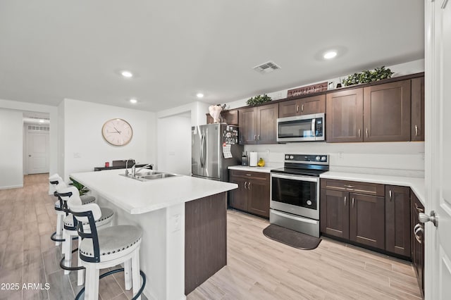 kitchen with appliances with stainless steel finishes, sink, light hardwood / wood-style flooring, and a kitchen island with sink