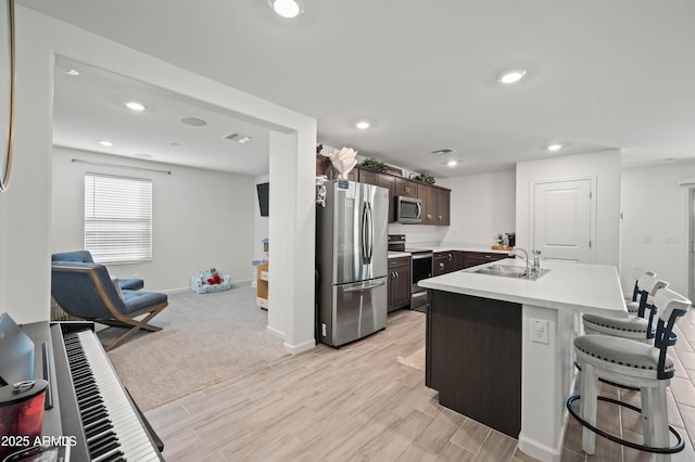 kitchen with a center island with sink, sink, dark brown cabinetry, appliances with stainless steel finishes, and a breakfast bar area