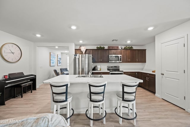 kitchen with a breakfast bar, dark brown cabinetry, stainless steel appliances, and an island with sink