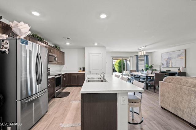 kitchen featuring light hardwood / wood-style floors, sink, an island with sink, stainless steel appliances, and dark brown cabinets