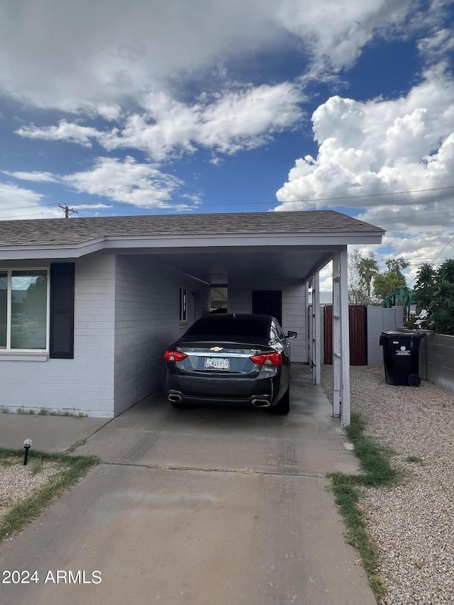 exterior space with concrete driveway, an attached carport, roof with shingles, fence, and brick siding