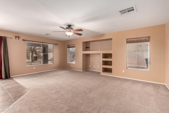 unfurnished living room featuring built in features, light colored carpet, visible vents, ceiling fan, and baseboards