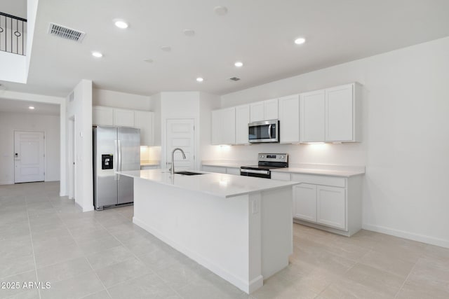 kitchen with appliances with stainless steel finishes, white cabinetry, sink, a kitchen island with sink, and light tile patterned floors