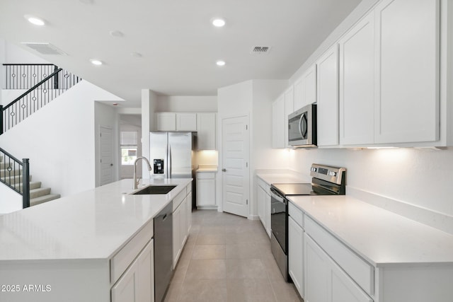 kitchen with sink, a center island with sink, light tile patterned floors, appliances with stainless steel finishes, and white cabinets