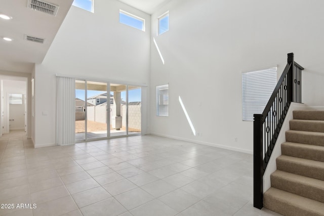 unfurnished living room with a towering ceiling, a healthy amount of sunlight, and light tile patterned floors